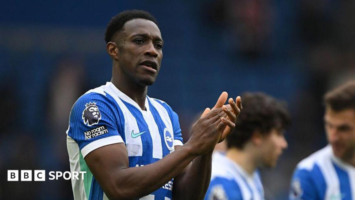Danny Welbeck, wearing a blue and white striped Brighton shirt, applauds