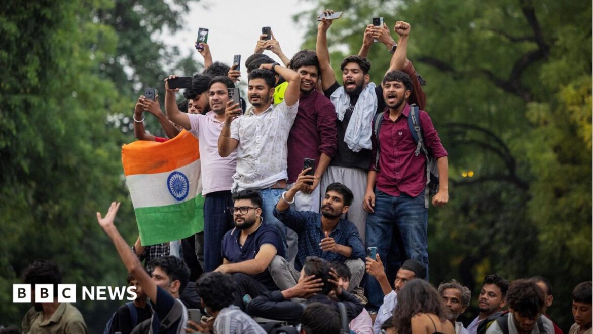 About a dozen people stand on an elevated platform celebrating, one holding an Indian flag