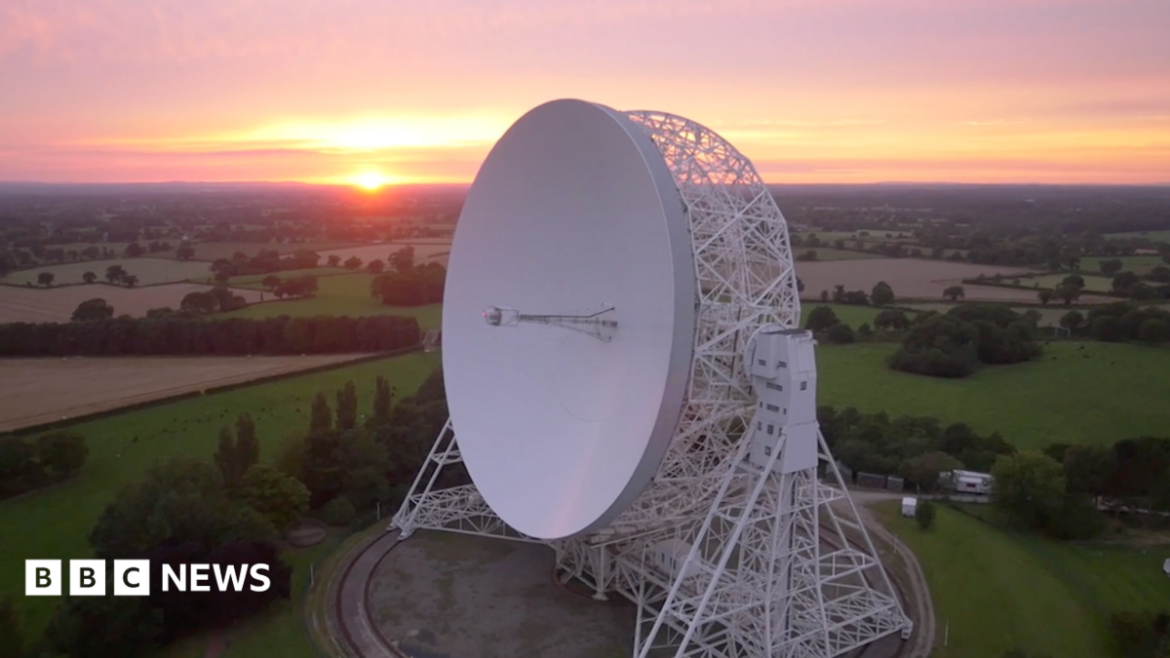 An aerial view at sunrise of the Lovell telescope at Jodrell Bank. Its huge white dish, taller than a house, is tilted