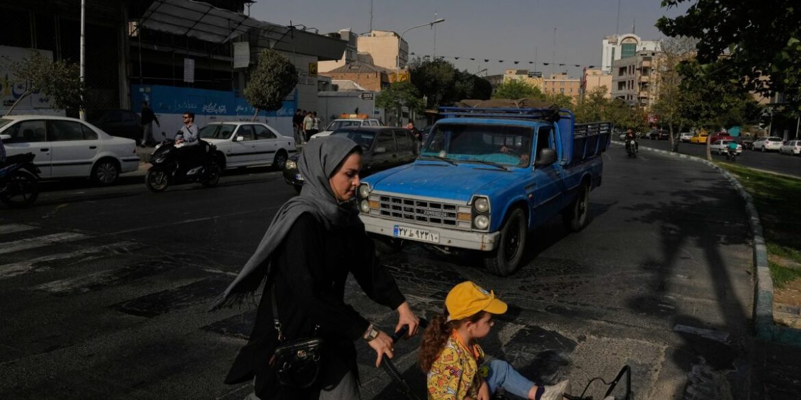 A woman crosses a street with a girl in downtown Tehran, Iran, Wednesday, July 22, 2026