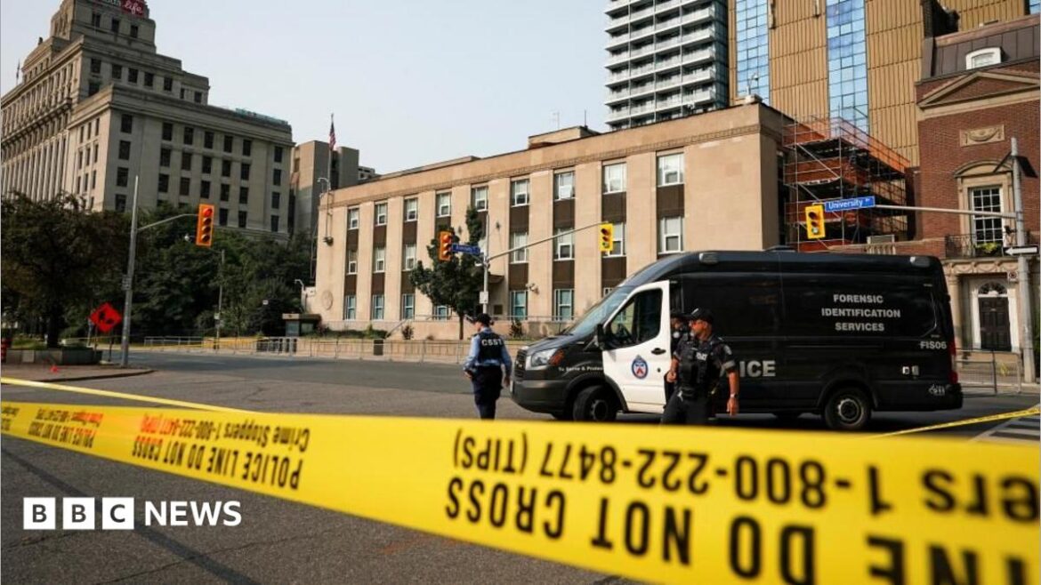 An image showing two Toronto Police officers standing behind yellow caution tape across a three-lane road. Behind them is a