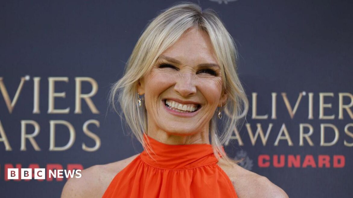 Jo Whiley poses on the red carpet at the Olivier Awards, wearing a bright orange sleeveless dress in front of an event