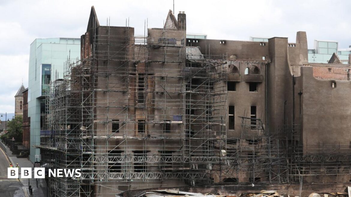 Large historic building undergoing restoration, surrounded by extensive metal scaffolding. The facade shows darkened