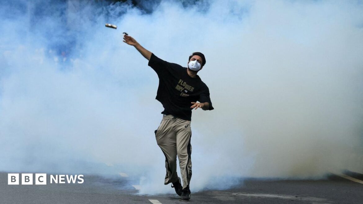 A protester throws back a tear gas canister toward police as supporters of the Cockroach Janta Party march on parliament on