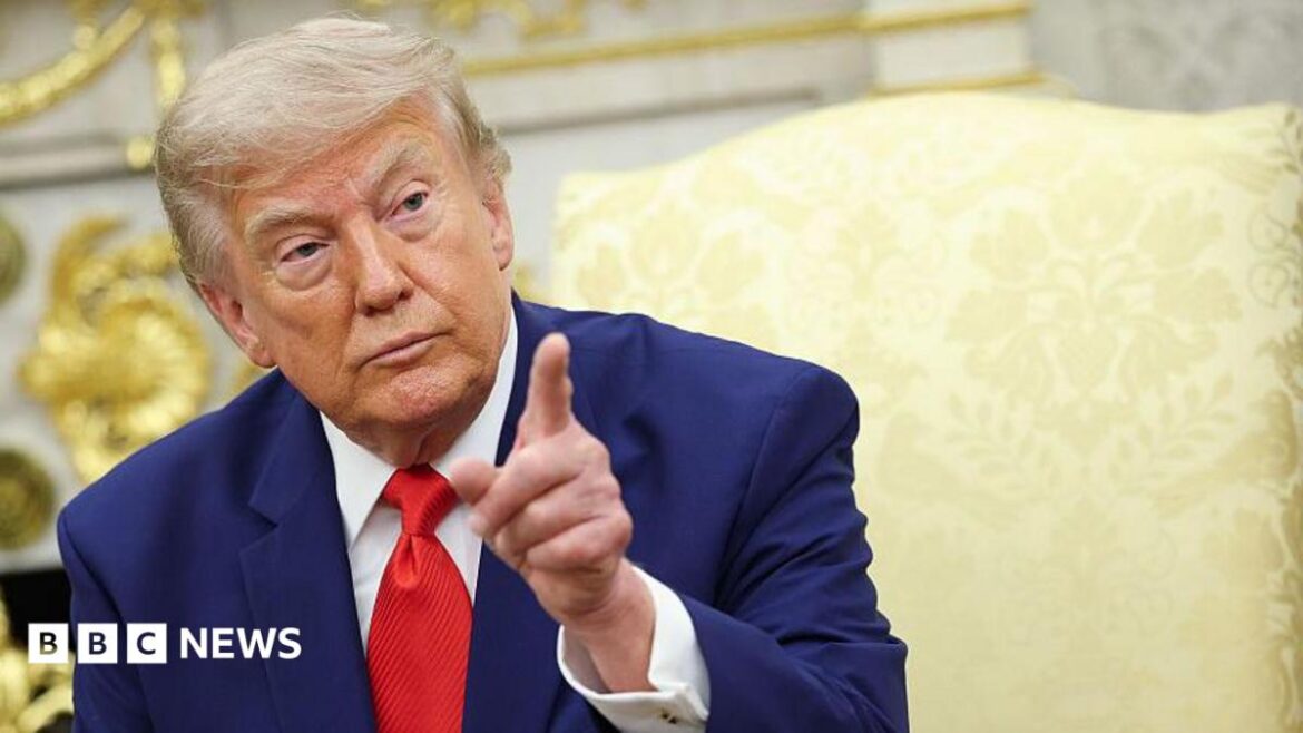 President Donald Trump pointing his finger. He has a serious look on his face and is wearing a blue suit with a white shirt