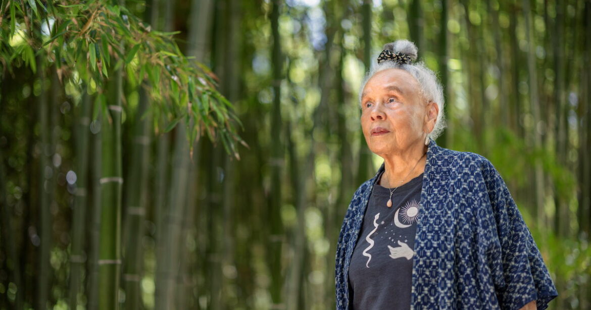 Artist Betye Saar, wearing a blue top, explores a bamboo grove in the Japanese Garden at The Huntington
