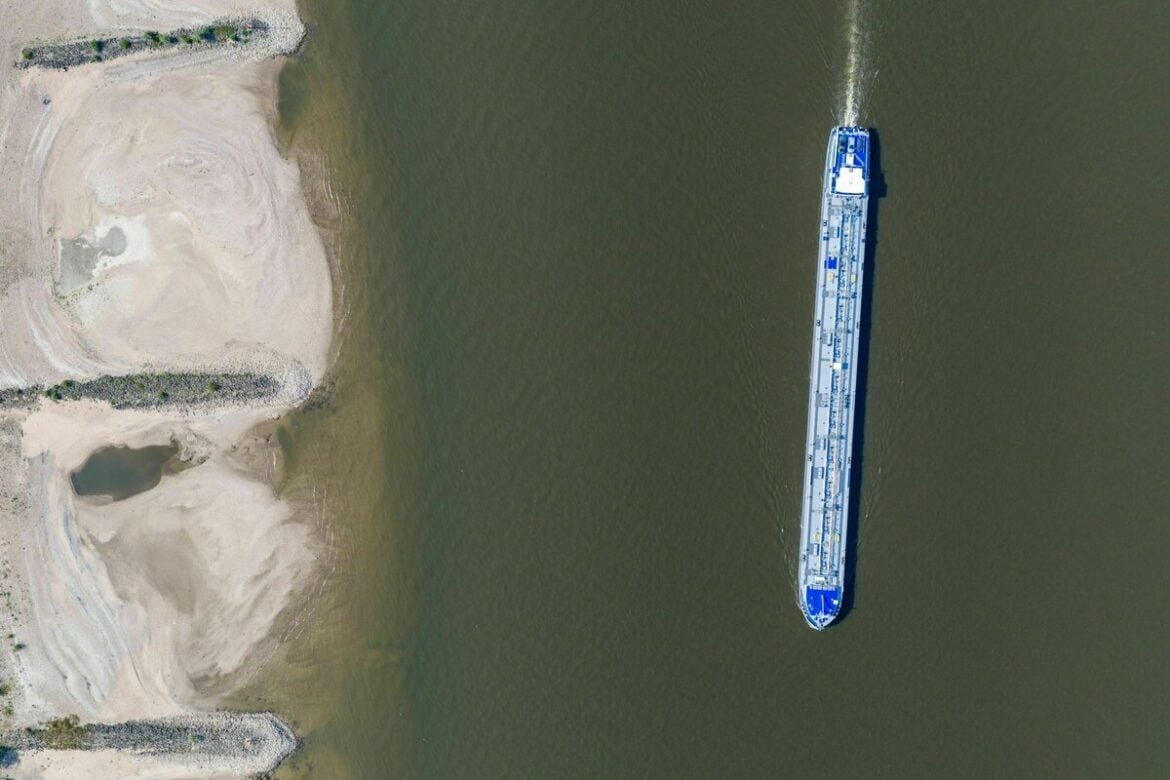 Am Rhein in Duisburg fährt ein Schiff in der Fahrrinne, am Ufer sind breite Sandbänke sichtbar, die bei normalem Wasserstand