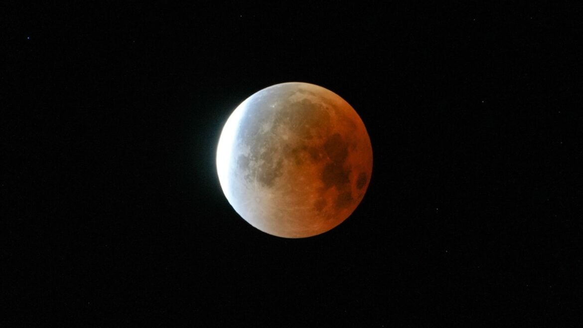 A full moon is shown in a black sky during a lunar eclipse, with its right side glowing red in Earth