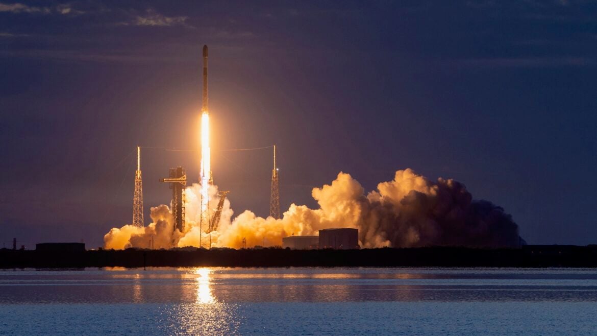 a black-and-white spacex falcon 9 rocket launches into a darkening evening sky
