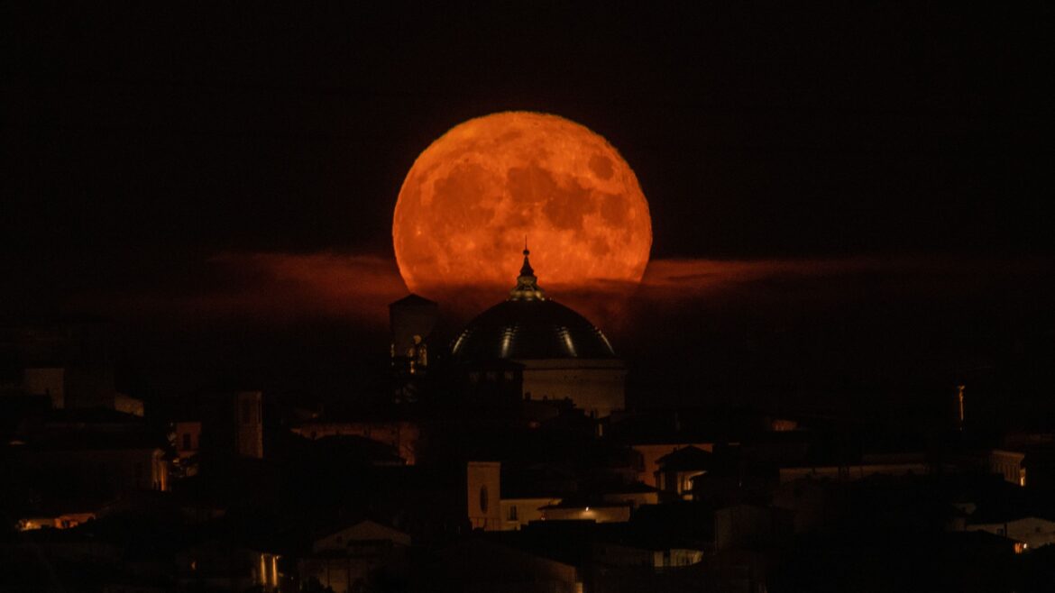 A red moon shines over an Italian toen in a black sky