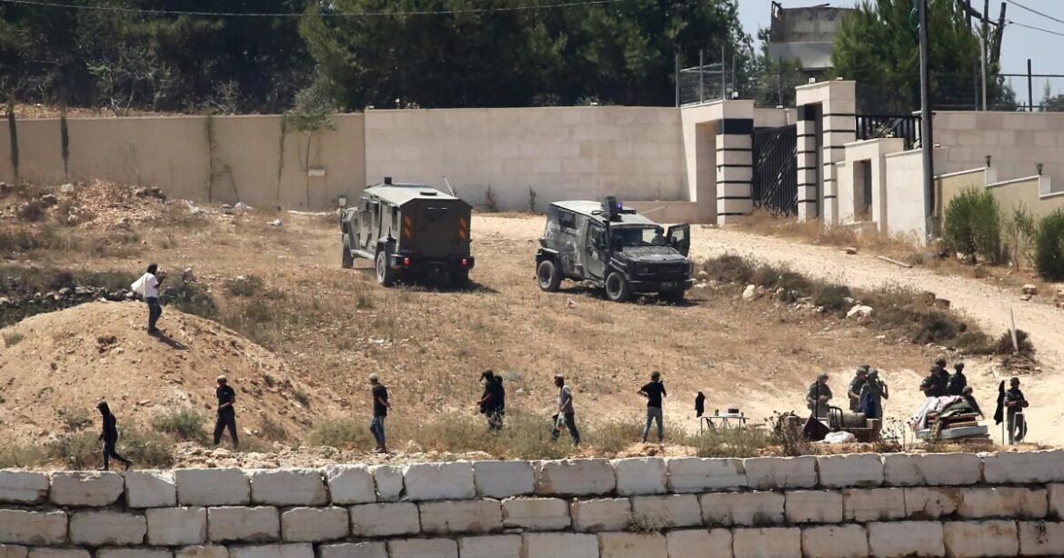 Israeli soldiers stand guard next to settlers in front of Palestinian homes that they have blockaded in the village of