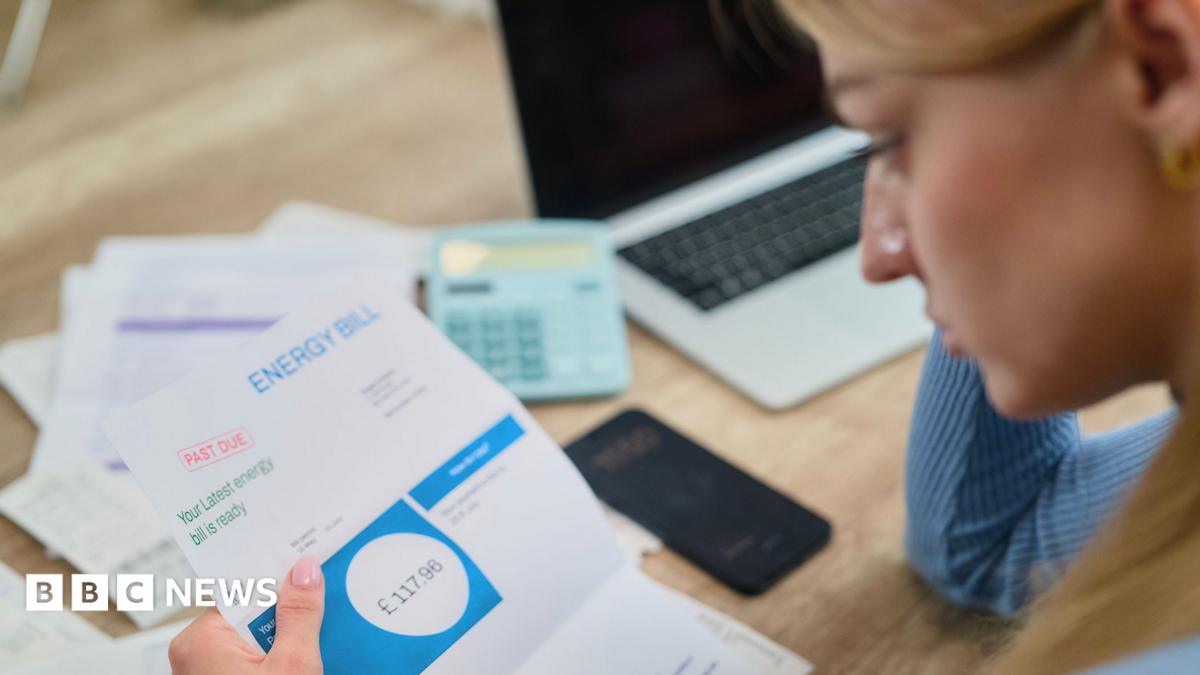 Woman looks at energy bill with paperwork, a calculator and a laptop on the table in front of her