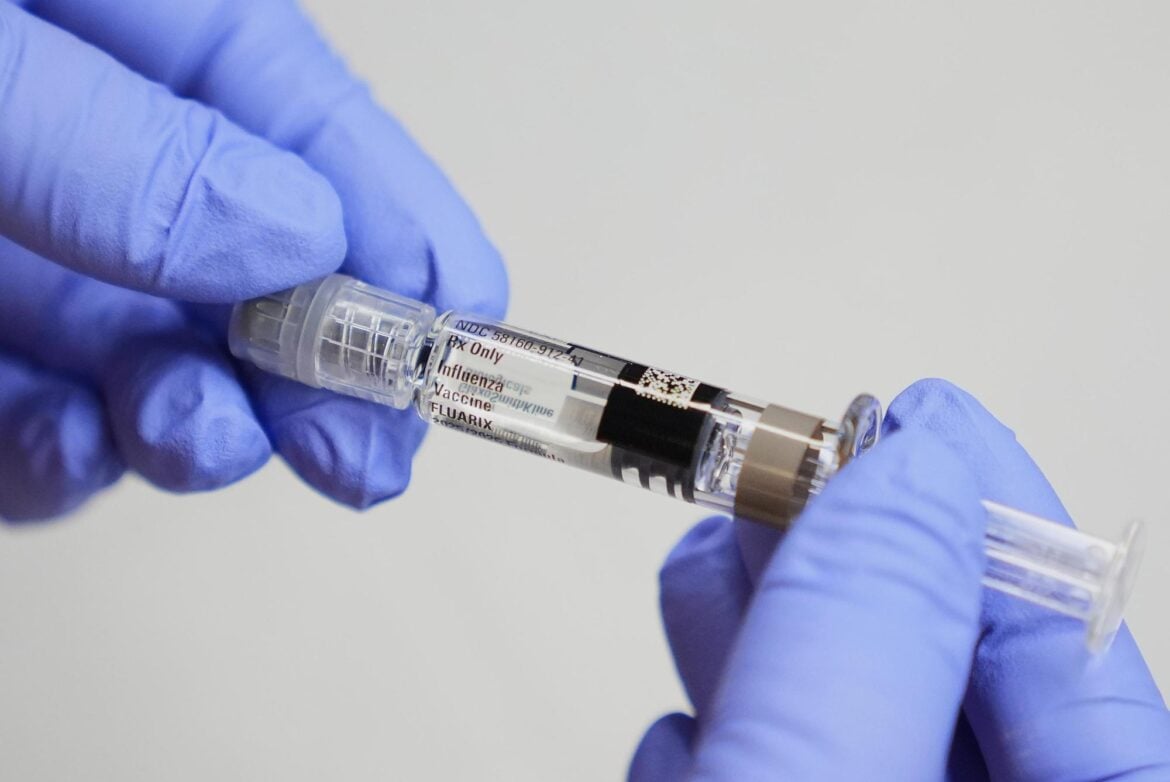 A certified medical assistant holds a syringe for a flu vaccine