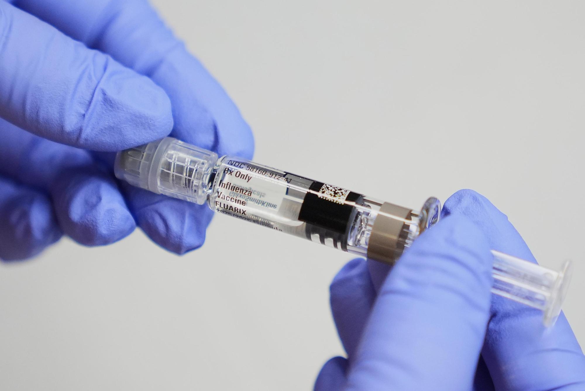 A certified medical assistant holds a syringe for a flu vaccine