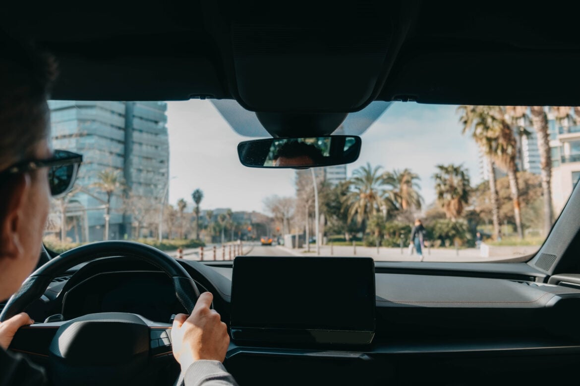 Ride-sharing driver navigating through a modern city with palm-tree-lined streets and urban buildings visible through the