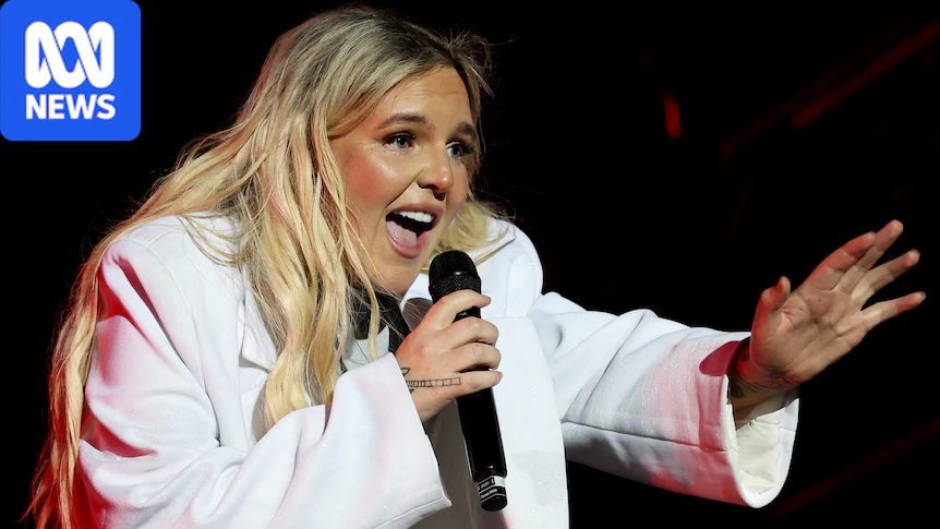 Tones And I performing at the Sydney Opera House in 2024. She's in a white jacket and holding a microphone