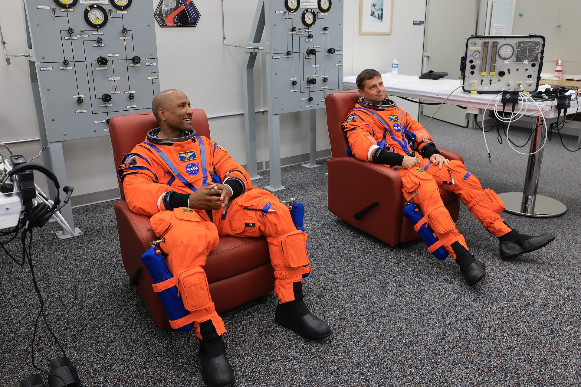 From left, NASA astronauts Victor Glover, Artemis II pilot and Reid Wiseman, Artemis II commander, are seated in chairs