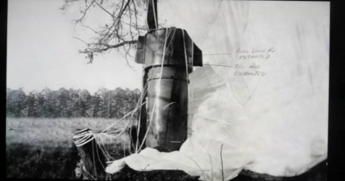 A large cylindrical bomb lying in an open field beside recovery equipment