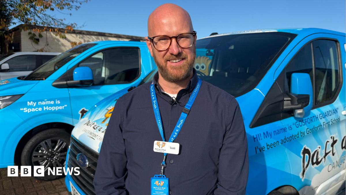 Scott Jobson, a man with a shaved head and beard who wears glasses, standing in front of the bright blue vans used by the