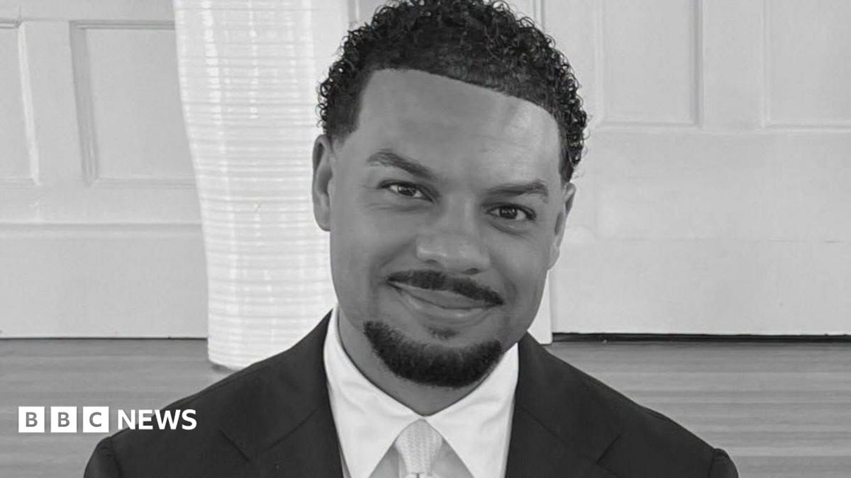 A black and white image of Cassius Newton, who has short, curly hair and is wearing a suit