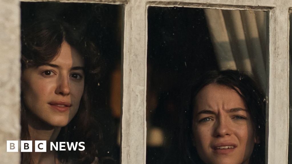 Daisy Edgar-Jones and Esme Creed-Miles peering out of a window in character as Elinor and Marianne Dashwood in Sense and