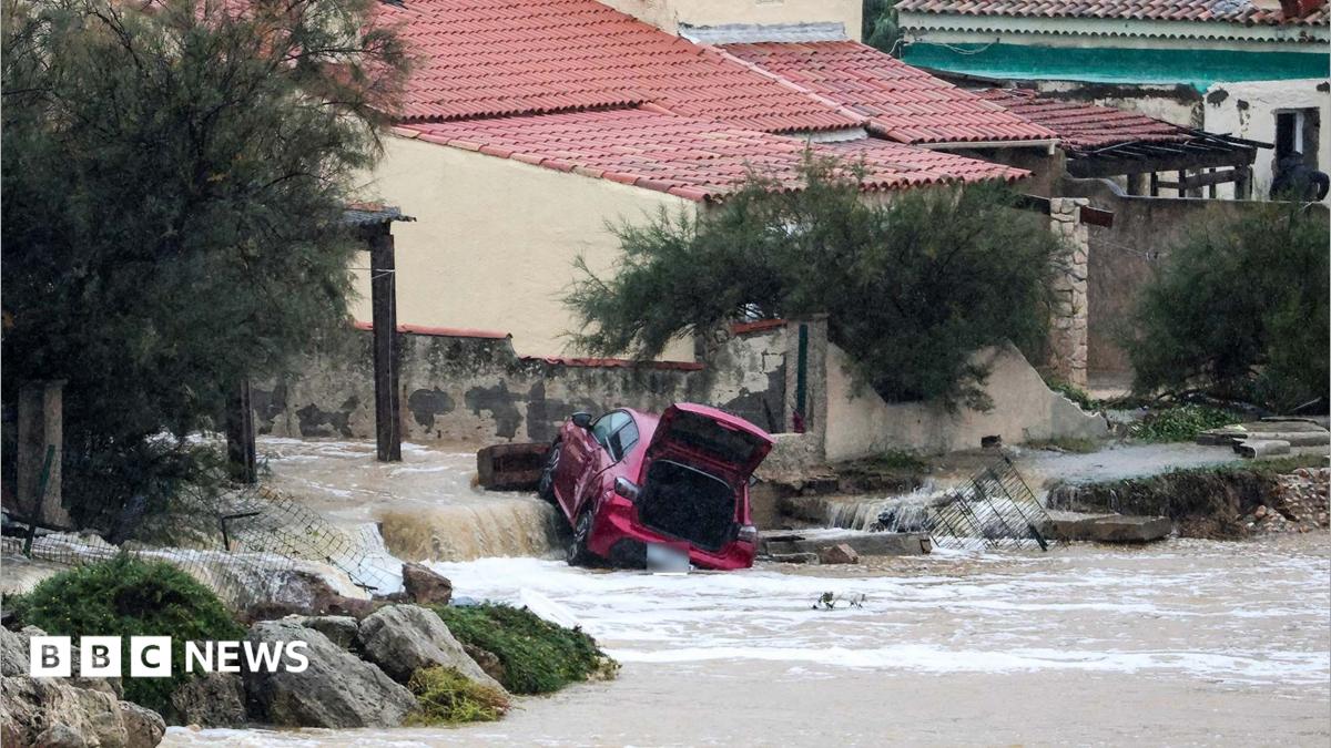 A damaged red car, lying at an angle with its boot open, in a flooded area