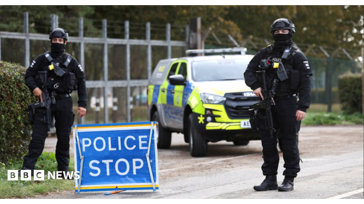 Armed police officers stand guard on a road outside the perimeter of the RAF Fairford airbase, after police declared a major