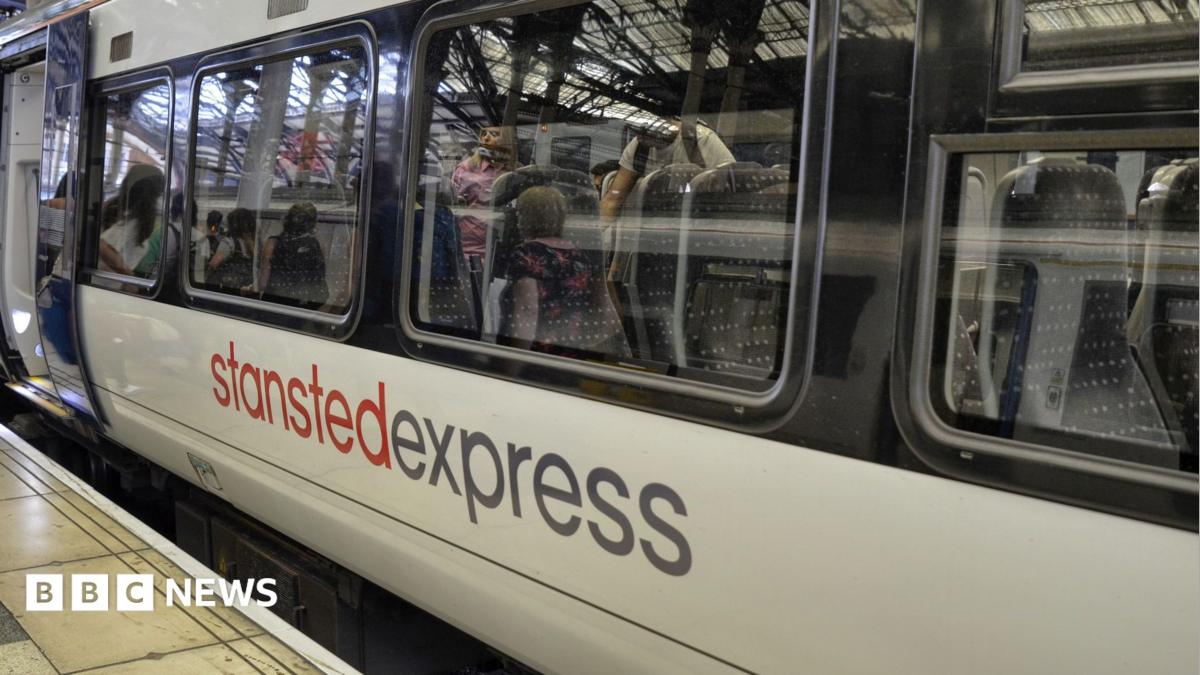 A Stansted Express train sits at the platform at London Liverpool station. Some passengers can be seen navigating the aisle