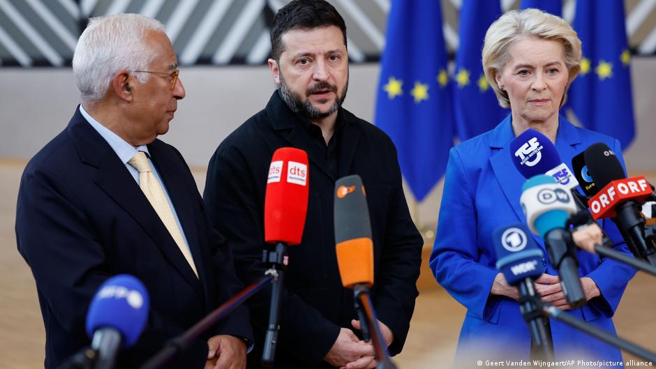 Antonio Costa, Volodymyr Zelenskyy and Ursula von der Leyen speaking into press microphones in front of EU flags