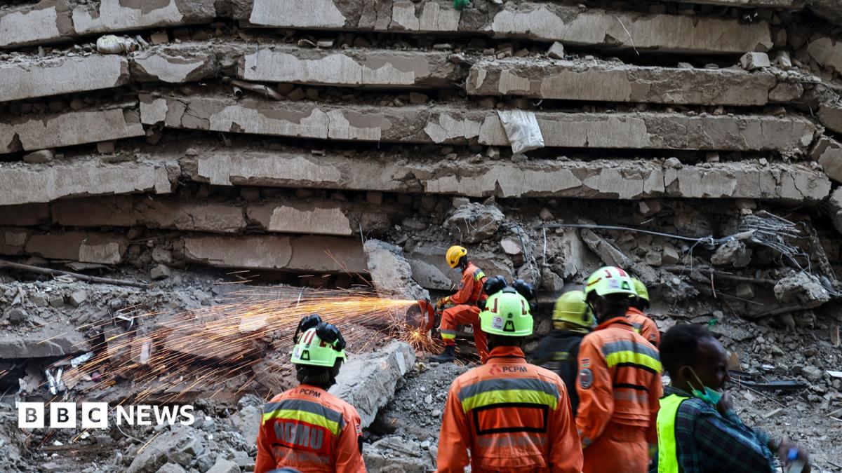 An emergency worker saws through metal and concrete as others watch on at the site of a building collapse in Nairobi
