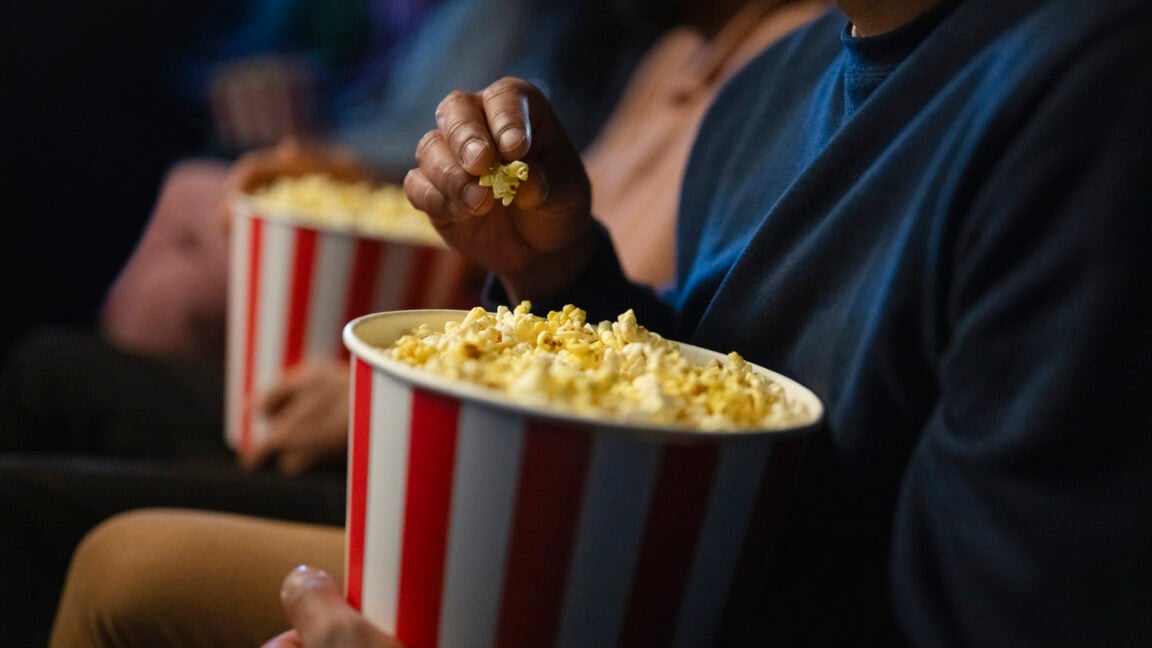 A close-up shot of a hand grabbing popcorn from a red and white striped container, symbolizing the enjoyment of a movie