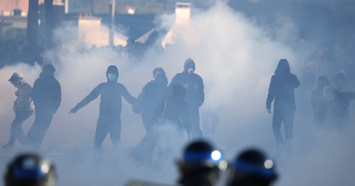French police officers operate in the foreground as demonstrators stand amid tear gas during student protests near the
