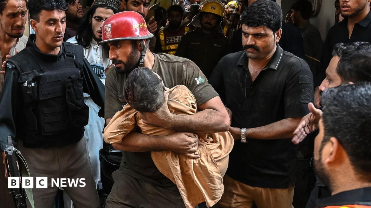 A rescue worker wearing a red helmet carries a small child as police officers, emergency responders and onlookers surround