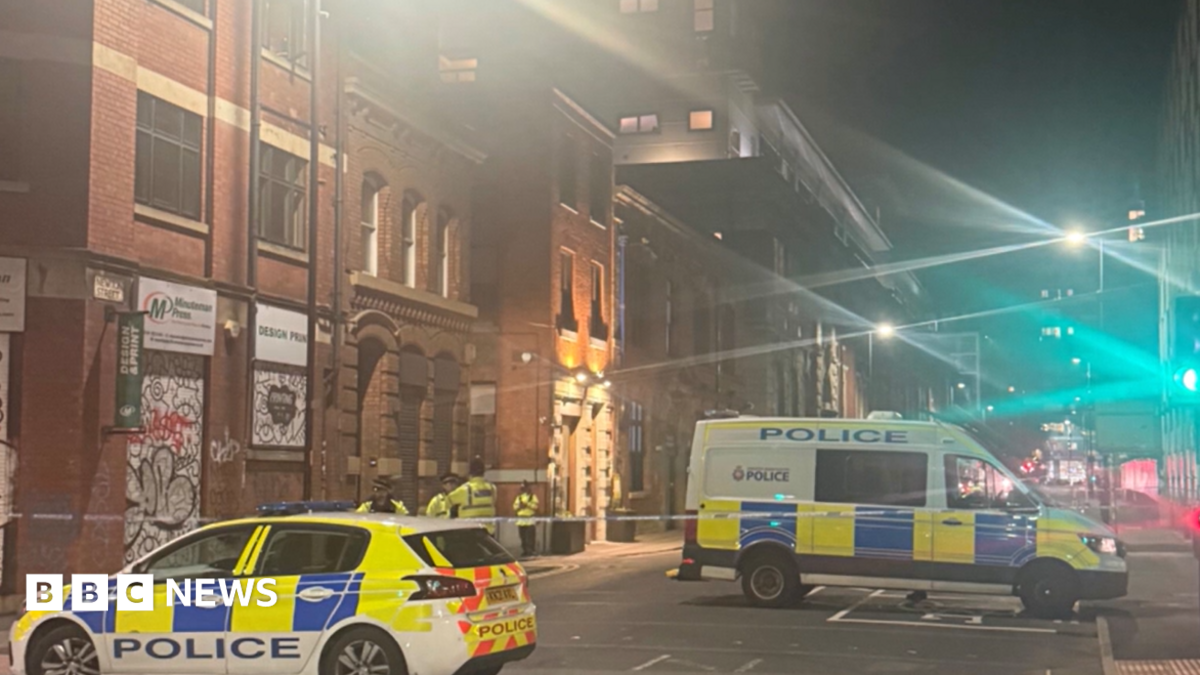A police car and a van and several officers stand guard by a police cordon in a city-centre location