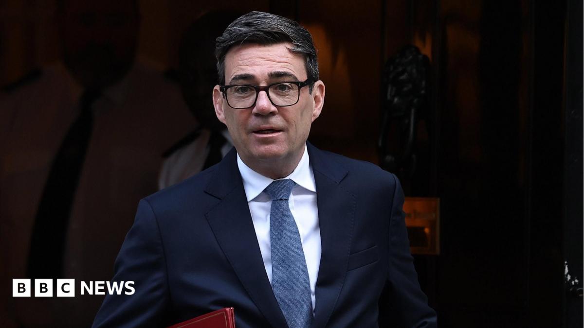 Andy Burnham leaving Downing Street. He is wearing a dark blue suit, blue tie and glasses. He is carrying a red folder