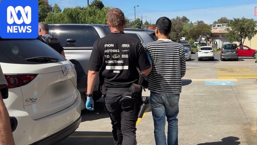 A police officer holds a man wearing a striped shirt by the arm