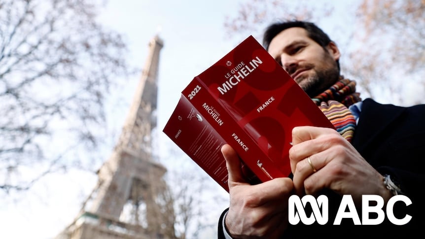 A man holding a Michelin Guide to France in front of the Eiffel Tower
