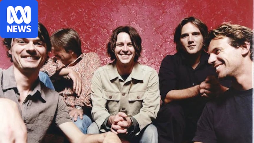 Five members of Powderfinger smiling and laughing on a red leather couch against a red patterned wall, in a posed group shot