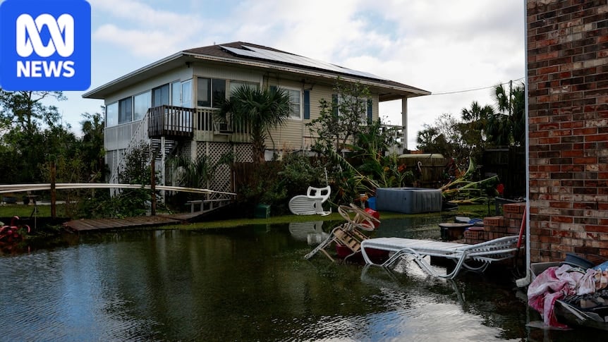 Floodwater fills a backyard with overturned patio furniture, in front of an elevated house