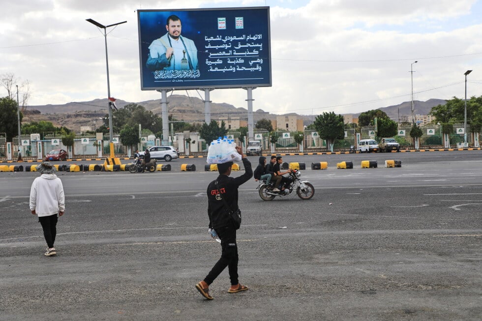 A vendor walks under a billboard showing Houthi leader Abdul Malik al-Houthi with a phrase that reads in Arabic: "The Saudi