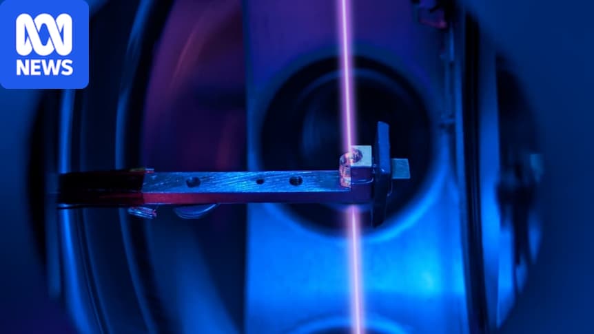Violet laser shining through a small crystal held in a metal clamp in a blue-lit lab
