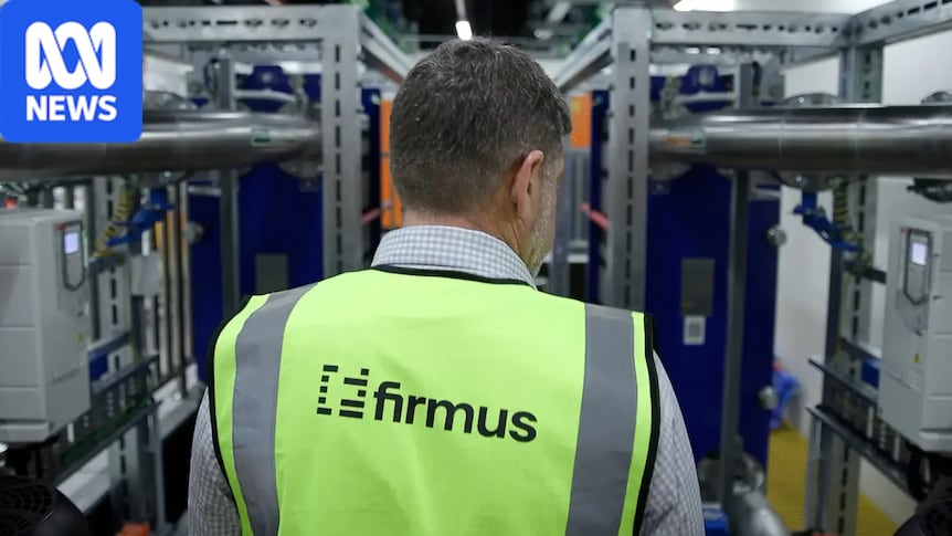 A man in a fluro vest with the word Firmus on it walks past shelves of computer equipment