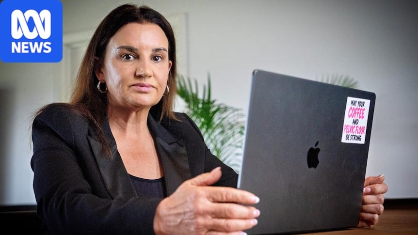 Jacqui Lambie sits at a wooden table in front of an open Apple MacBook laptop