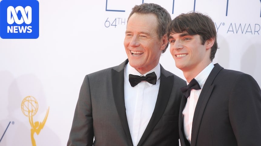 two men smile on a red carpet
