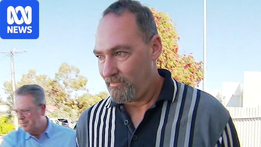 reporters point their mics towards a man in a stripe top walking on a suburban street