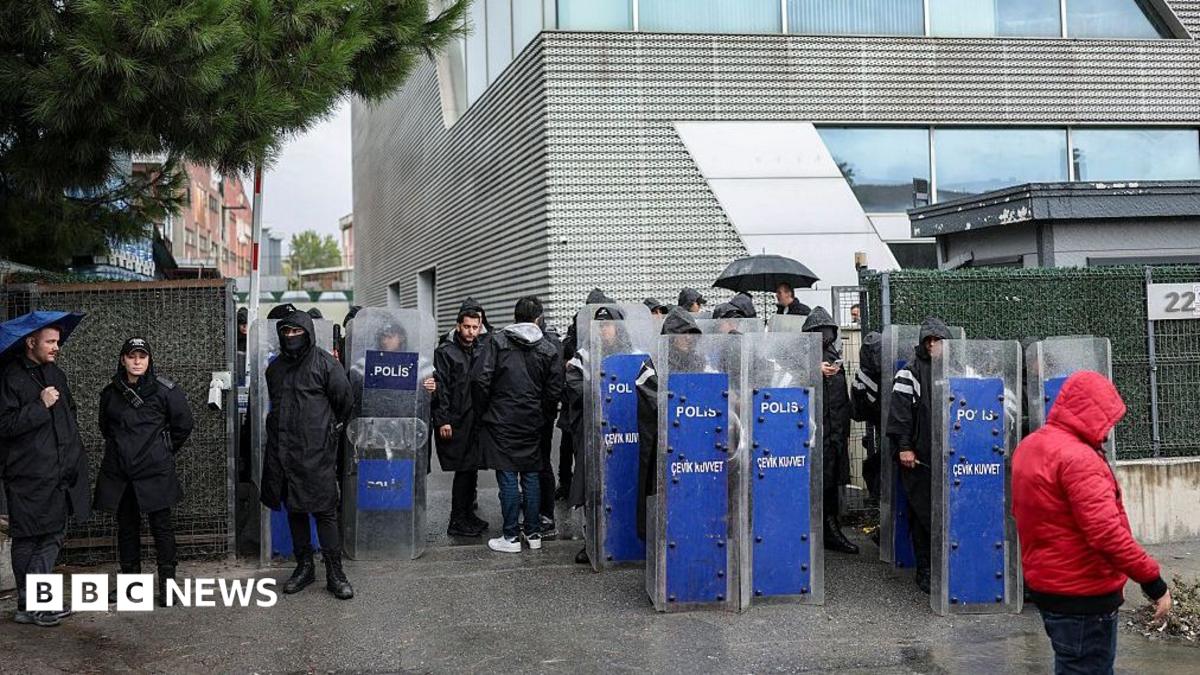 A row of riot police stood outside in the rain outside a grey office building