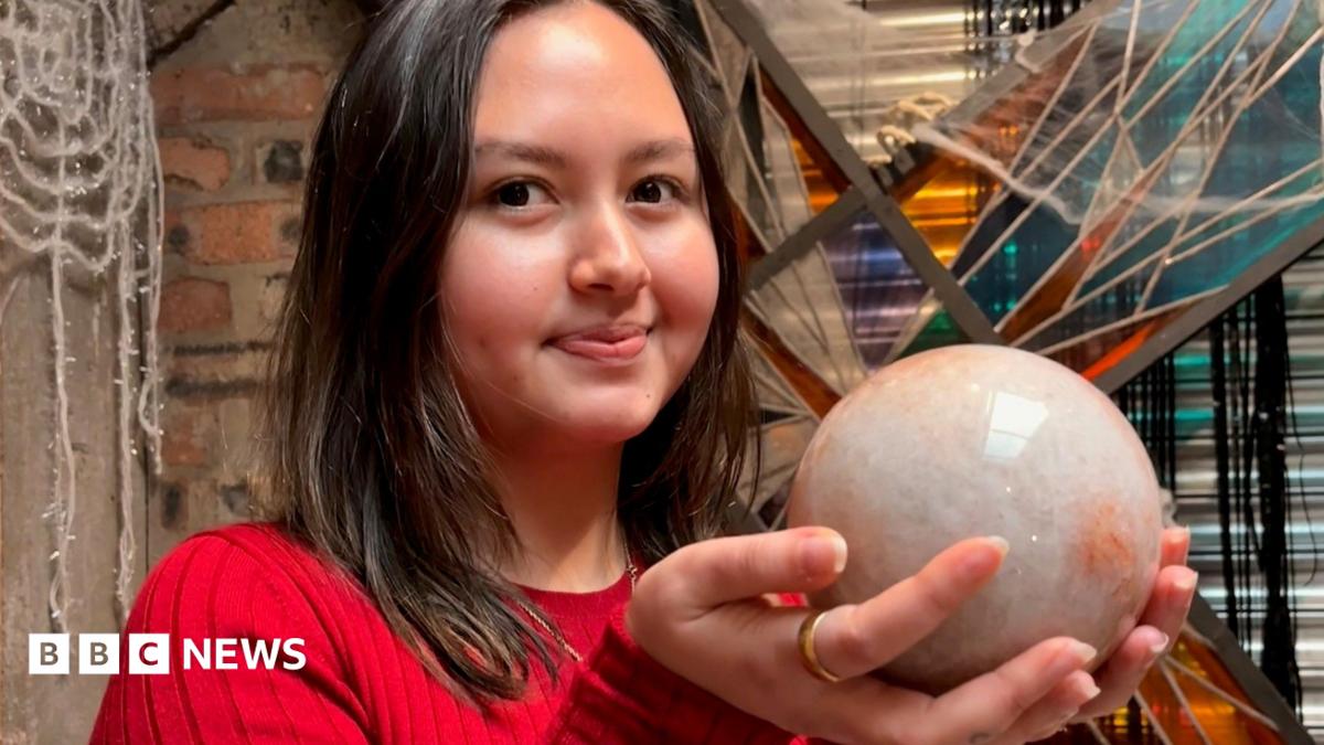 A young woman with short dark hair, smiling while holding a orange circular crystal