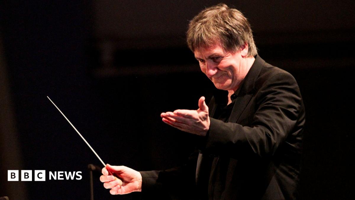 George Fenton conducts an orchestra, with a baton in his hand
