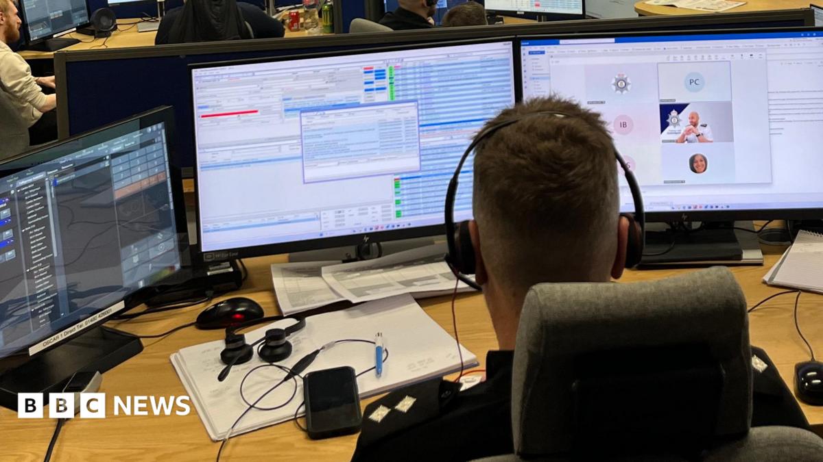 A man is sitting in an office with his back to the camera. He has three computer screens in front of him, each showing