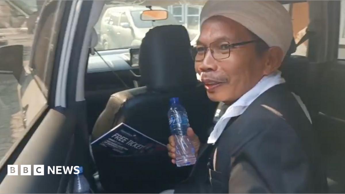 A man, holding a water bottle, is getting out of the back seat of a car
